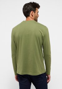 Långärmad skjorta i olivgrön bomull med rund halsringning, slät textur och rak nederkant. Bärs med mörkblå jeans.