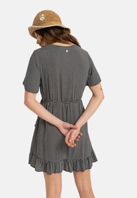 Black and white patterned dress with short sleeves, a fitted waist, and a ruffled hem. Model is wearing a straw hat with floral accent.