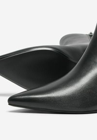Bottes de cheville noires à bout pointu avec une finition brillante. Elles présentent un dessus lisse et une semelle texturée, mettant en avant un design moderne et épuré.