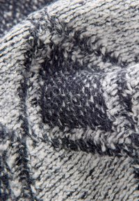 Tela de punto en tonos de gris oscuro y crema, con un patrón texturizado y una superficie suave y esponjosa con fibras visibles.