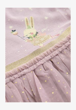 Tecido lila con una textura acanalada que presenta un diseño de conejo. Ribete dorado y un volado de tul en la parte inferior con pequeños lunares dorados.
