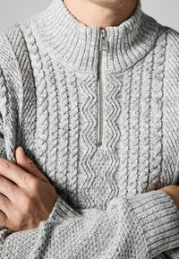 Gray knit sweater with a high collar and zip closure, featuring textured cable and zigzag patterns, ribbed cuffs, and a soft texture.