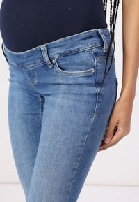 Graviditetsjeans i lys blå denim med en jevn tekstur, med en bred midje og klassisk fem-lomme design.