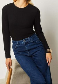 Haut noir à manches longues côtelé associé à un jean en denim bleu taille haute. La tenue présente un col rond et une texture lisse.