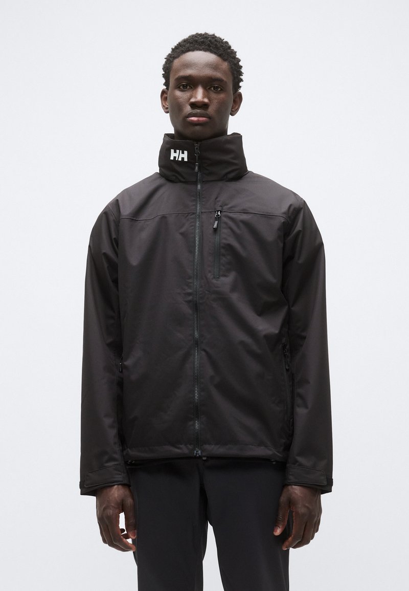 Chaqueta impermeable negra con cuello alto, cremallera frontal y bolsillo en el pecho con cremallera; incluye el logo de la marca en el cuello. Textura lisa.