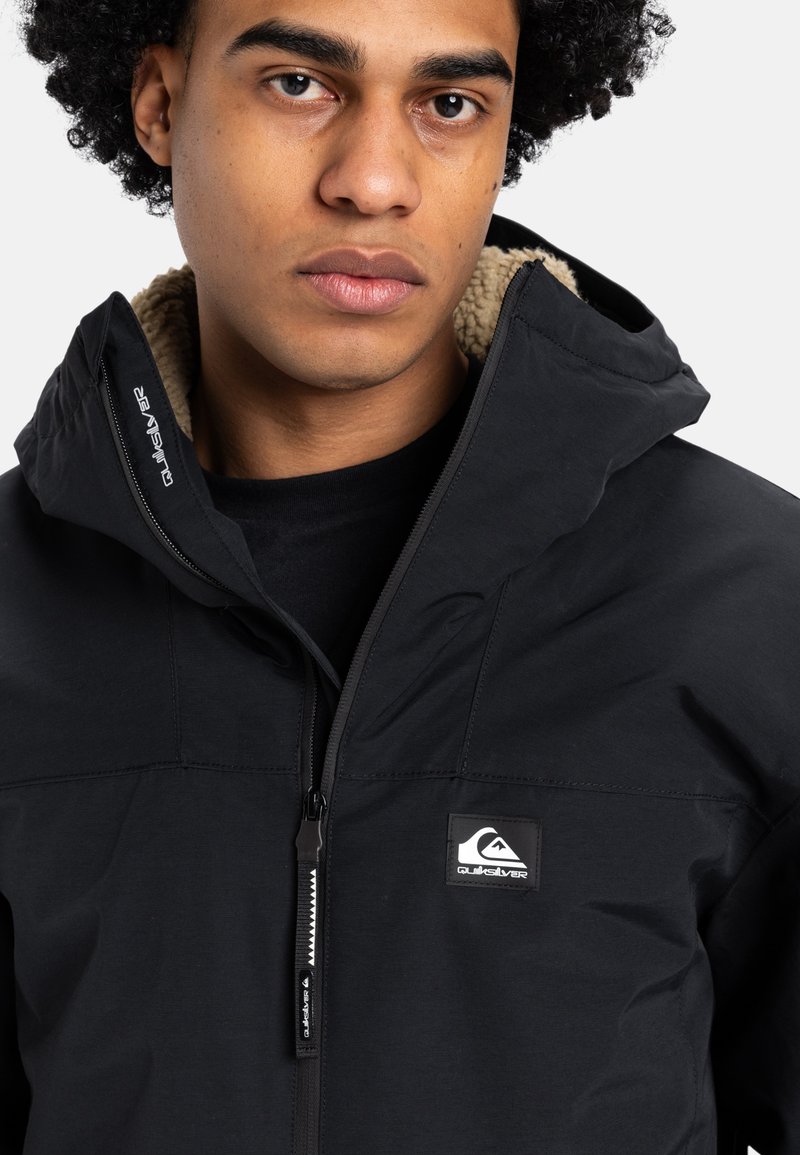 Czarna kurtka z zamkiem błyskawicznym i kapturem, z miękką podszewką, logotypem Quiksilver i teksturowanym materiałem. Zamek błyskawiczny z przodu oraz regulowane elementy.
