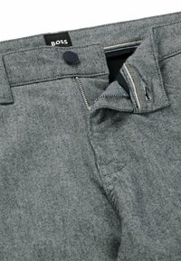 Pantalons en denim gris avec une fermeture éclair, un bouton de fermeture et une étiquette de marque noire. Comprend des coutures structurées et une texture de tissu de poids moyen.