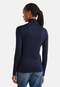 Top de cuello alto de manga larga en color azul marino, fabricado en un tejido suave, con un diseño ajustado y un cuello alto. Combinado con unos vaqueros de mezclilla azules.