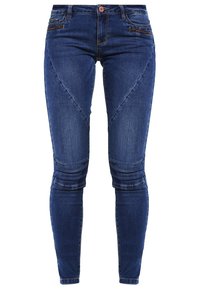 Jeans de mezclilla azul de corte ajustado con una textura suave, que presentan detalles de costuras en ángulo y bolsillos frontales con cremallera.