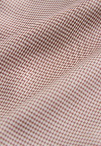 Tissu marron et blanc à petit motif pied-de-poule avec des plis doux et une texture visible en vue rapprochée.