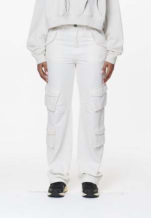 Pantalones cargo blancos de mezclilla, con múltiples bolsillos laterales, un corte relajado y costuras resistentes. Combinados con zapatillas deportivas negras.