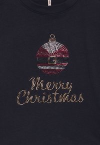 Sötétkék póló csillogó karácsonyi díszítéssel, piros, fehér és arany strasszokkal. Szöveg: "Boldog Karácsonyt" arany strasszokkal.
