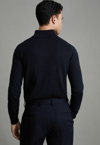 Pull en laine bleu marine avec col, doté de manches longues et d'une coupe ajustée. Associé à un pantalon sombre, mettant en valeur une texture lisse.