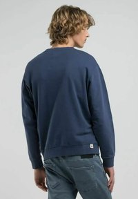 Felpa blu navy realizzata in cotone, con una vestibilità rilassata, polsini a coste e una piccola etichetta con logo all'orlo. Texture morbida visibile.