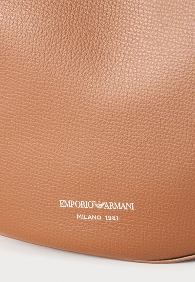 Surface en cuir texturé marron avec logo Emporio Armani blanc et texte "Milano 1981" embossé près du bas.
