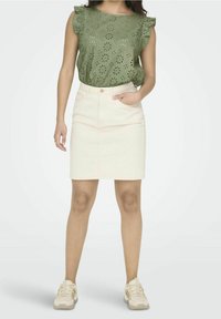 Top verde chiaro in pizzo con maniche a volant, abbinato a una gonna di jeans rosa chiaro con tasca frontale e chiusura a bottoni. Sneakers beige.