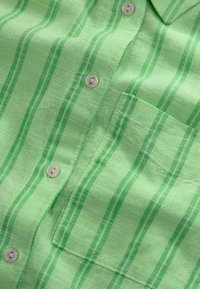 Camicia a maniche corte a righe verdi, realizzata in tessuto leggero, con taschino, bottoni perla e righe alternate di verde scuro e verde chiaro.