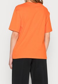 Pomarańczowy bawełniany t-shirt z krótkimi rękawami i luźnym krojem, z okrągłym dekoltem i gładkim wzorem, widoczny od tyłu.