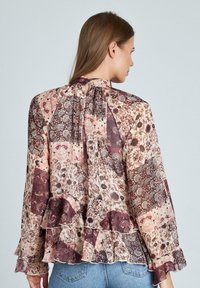 Gemusterte Bluse aus weichem Stoff mit langen, ausgestellt geschnittenen Ärmeln, Rüschensaum und schlüssellochförmigem Rückendetail in Beigetönen, Burgunder und Creme.