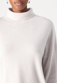 Jasnoszary golfowy sweter wykonany z miękkiego, strukturalnego materiału. Posiada wysoki kołnierz i luźny krój z opadłymi ramionami.
