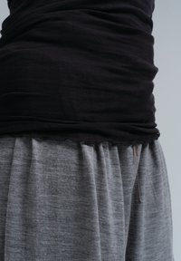 Čierny priliehavý top s nahrnutou látkou na leme, kombinovaný so šedými plisovanými nohavicami. Mäkka textura s viditeľnými šviami.