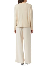 Beżowy sweter z dzianiny z długimi rękawami, okrągłym dekoltem i prostym krojem. Połączony z szerokimi beżowymi spodniami o miękkiej fakturze tkaniny.