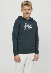 Felpa con cappuccio blu scuro realizzata in morbido tessuto, con stampa del logo frontale, cappuccio con coulisse e polsini a costine, abbinata a pantaloni della tuta grigi chiari.