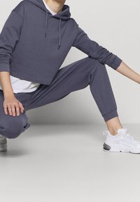 Gray cropped hoodie with a hood and long sleeves, paired with matching joggers. Features elastic cuffs and a white t-shirt underneath. White sneakers.