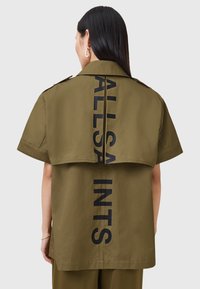 Khaki koszulka z krótkim rękawem z dużym czarnym nadrukiem "ALLSAINTS" na plecach, w luźnym kroju i gładkiej teksturze tkaniny.