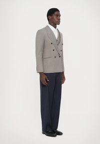 Szürke, dupla soros blazer fekete gombokkal, tengerészkék csíkozott, bő szárú nadrággal és fekete cipővel párosítva, egy fehér ing felett viselve.