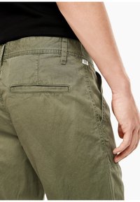 Chinos vert olive avec une texture lisse, dotés d'une poche arrière et d'un détail d'étiquette sur la ceinture. Design classique avec une coupe ajustée.