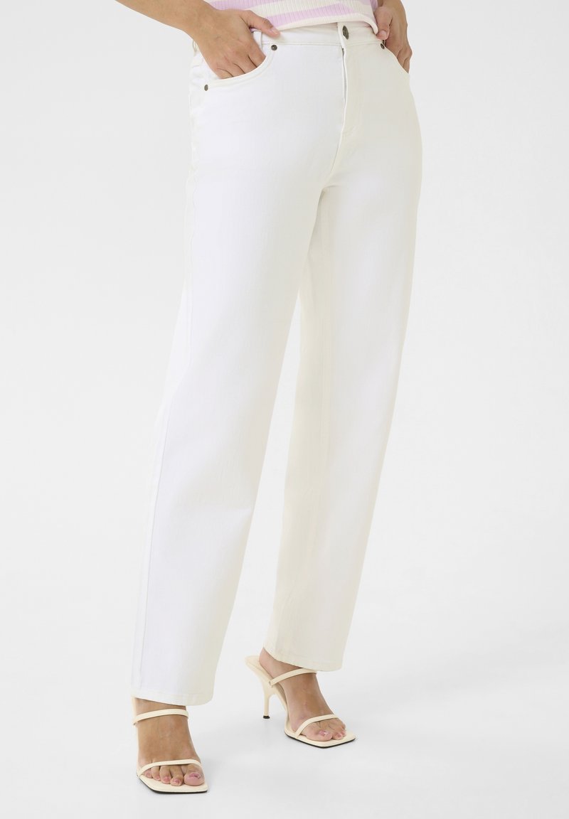 Jeans de denim blanco con corte recto, cinco bolsillos, cierre frontal con botón y detalle de costura sutil. Combinados con tacones ligeros y con tiras.