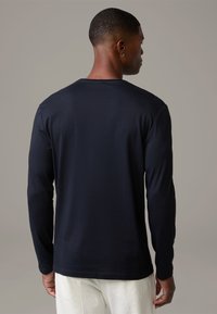 Long-sleeve navy shirt made from soft cotton. Features a round neckline and a relaxed fit, with a smooth texture and minimal stitching details.