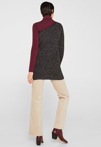 Zwarte en grijze gemarmerde tuniek met een bordeauxrode coltrui. Beige corduroy broeken. Bruine hoge laarzen. Over het algemeen een ontspannen pasvorm ontwerp.