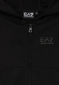 Felpa nera con zip realizzata in tessuto morbido. Presenta tasche a marsupio, un cappuccio e un logo EA7 testurizzato di colore verde scuro sul petto.