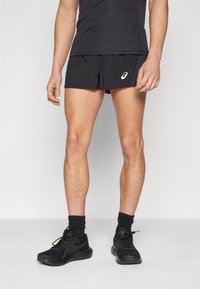 Black athletic shorts with a white logo, made from lightweight fabric. Worn with a fitted black shirt and black running shoes.