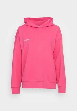 Sweat à capuche rose vif à manches longues avec un petit texte blanc sur la poitrine gauche indiquant « LÀ OÙ LA VIE COMMENCE ET L'AMOUR NE FINIT JAMAIS. »
