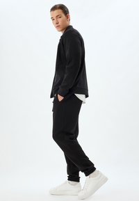 Schwarzes Sweatshirt und Jogginghose aus weichem Stoff, kombiniert mit weißen Turnschuhen. Das Design umfasst elastische Bündchen und eine lockere Passform.