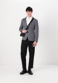 Γκρι υφασμάτινο σακάκι πάνω από λευκό πουκάμισο, μαύρο παντελόνι και μα�ύρα παπούτσια. Φοράει μια μικρή μαύρη τσάντα διαγώνια.