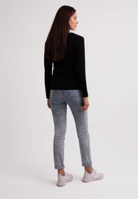 Sort langærmet sweater parret med lys blå, let slidte skinny jeans og hvide atletiske sneakers. Glat tekstur, tætsiddende design.