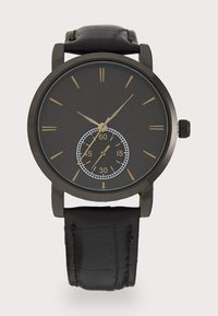 Black watch with a round face, gold hour markers, and a subdial displaying seconds. Features a black leather strap with a textured finish.