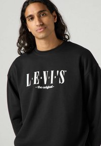 Felpa nera in cotone con testo bianco in bold "LEVI'S the original" sul davanti, design semplice con girocollo e vestibilità rilassata.