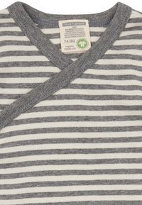 Grau-weiße gestreifte Wickelbluse aus Bio-Baumwolle, mit einem überkreuzten Ausschnitt und weichem Griff, mit sichtbarem Pflegeetikett.