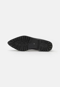 Suela de zapato de goma negra con surcos de tracción profundos y una forma suave y curva. Talla marcada como "37" en el talón.