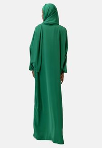Grön lång klänning med svällande ärmar och en matchande hijab, gjord av ett glatt tyg. Designen är enkel och har en flytande silhuett.