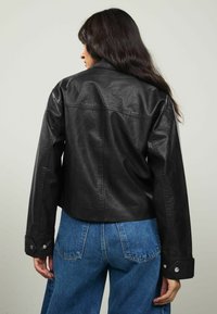 Zwarte faux leren jas met een cropped ontwerp, voorzien van knoopmanchetten en een gladde textuur, gecombineerd met high-waisted spijkerbroeken.