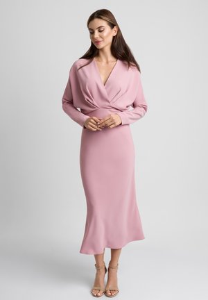 Długa różowa sukienka z dekoltem w serek i długimi rękawami, z zebranym stanikiem i zwiewną spódnicą. Gładka faktura i elegancka sylwetka.