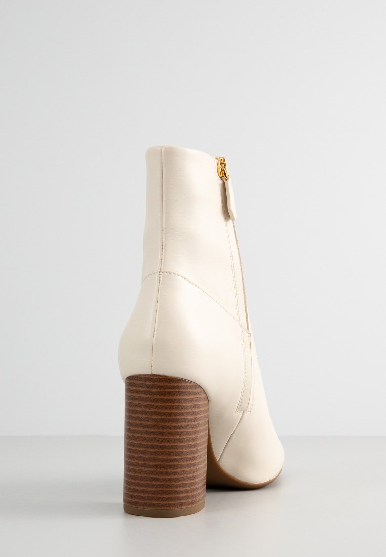 Stivaletto in pelle beige con punta rotonda, tacco a blocco in legno rigato e dettaglio della cerniera dorata sul retro. Texture liscia e design minimale.