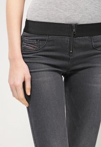 Grå jeans med ett stretchigt midjeband, dragkedja och en höftficka med en liten röd detalj. Slät textur och slim fit-design.