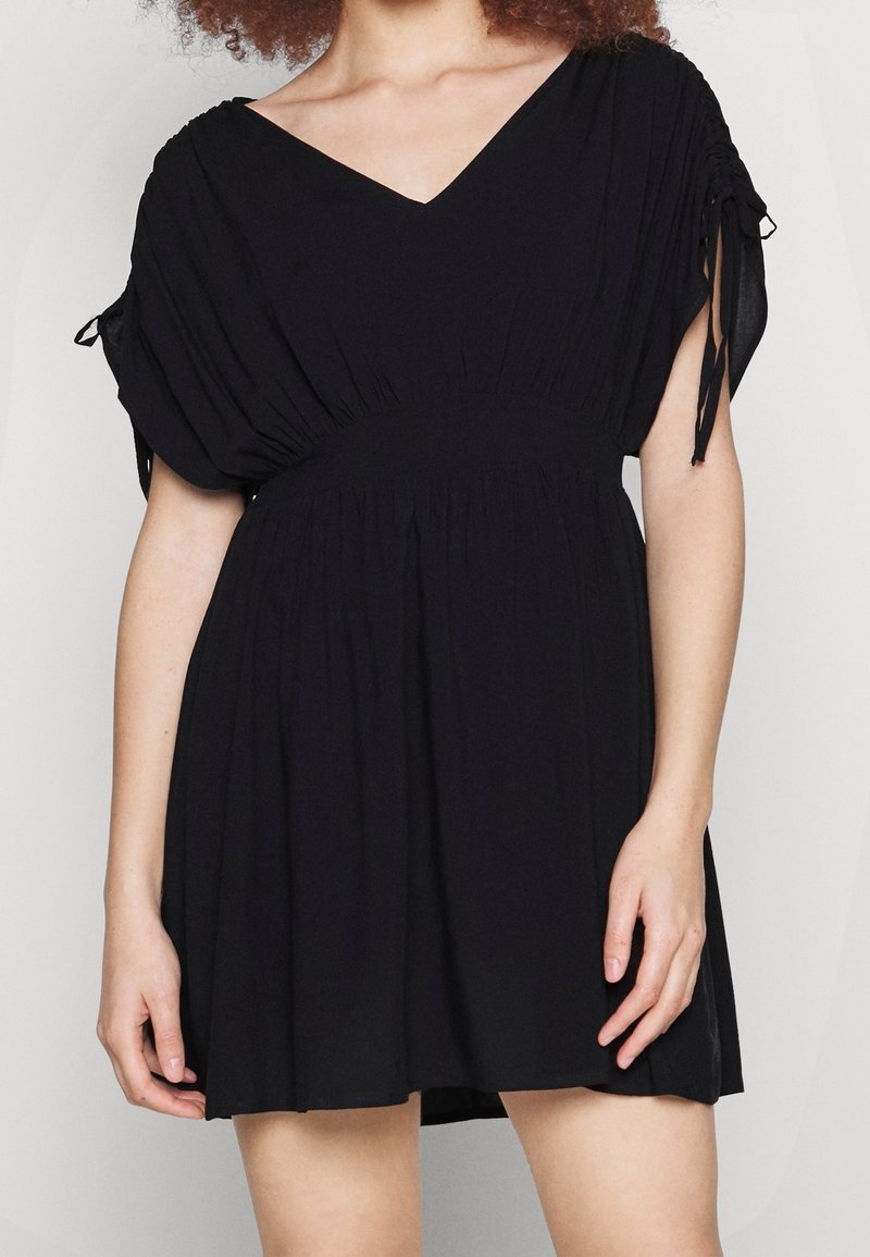 Robe noire avec un décolleté en V, des manches bouffantes courtes avec liens, et une taille froncée, fabriquée à partir d'un tissu léger pour un ajustement décontracté.